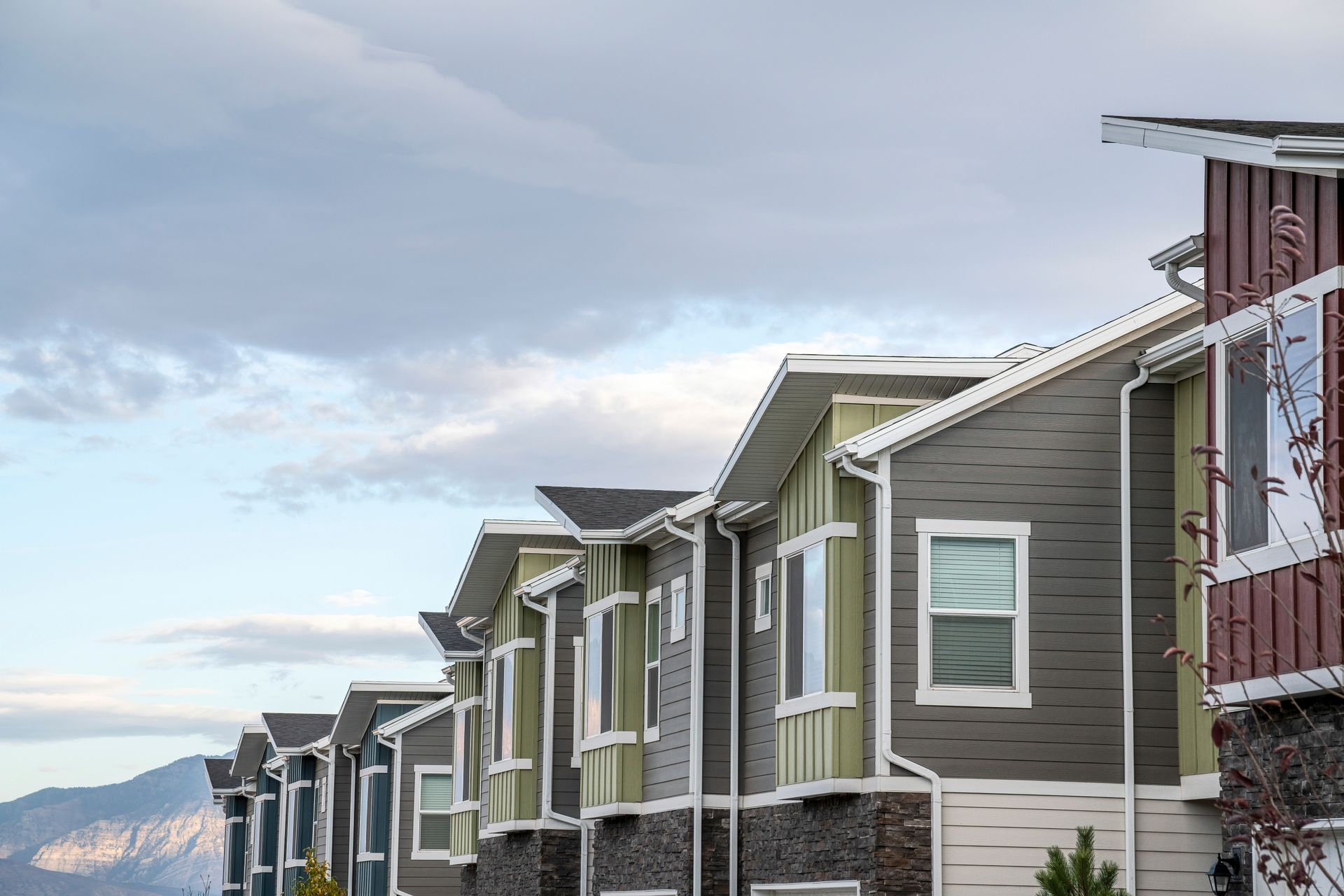 Row of modern townhouses with gray siding and snowy mountain backdrop under a cloudy sky