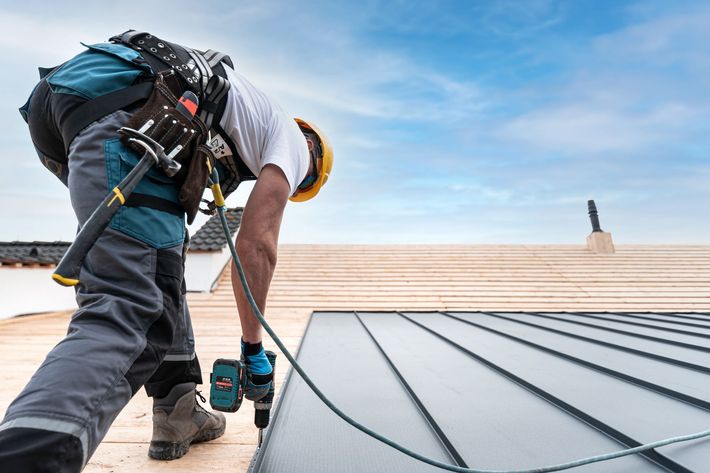 Worker installing metal roofing on a rooftop under a blue sky Worker installing metal roofing on a rooftop under a blue sky