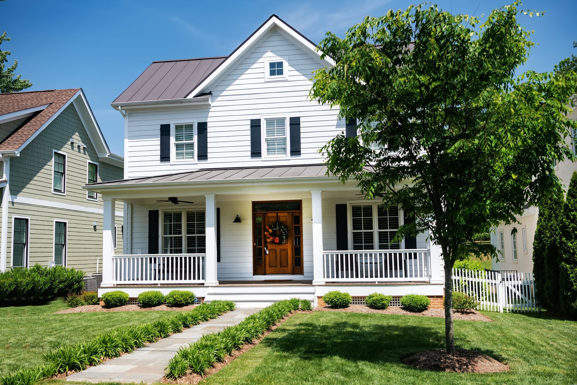 White two-story house with front porch, green lawn, and a tree in the yard