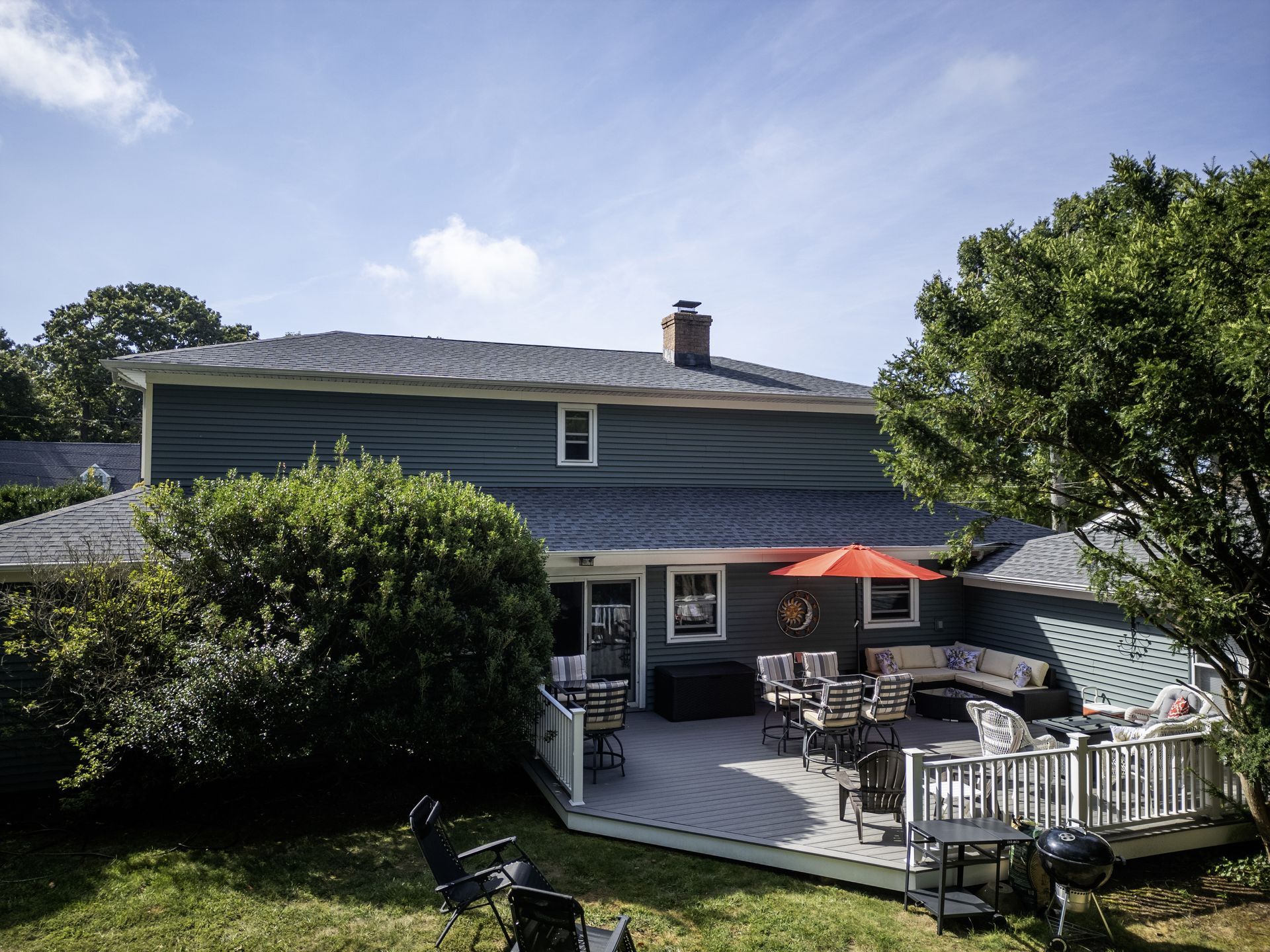 Backyard deck with outdoor furniture, orange umbrella, and a two-story house under a sunny sky