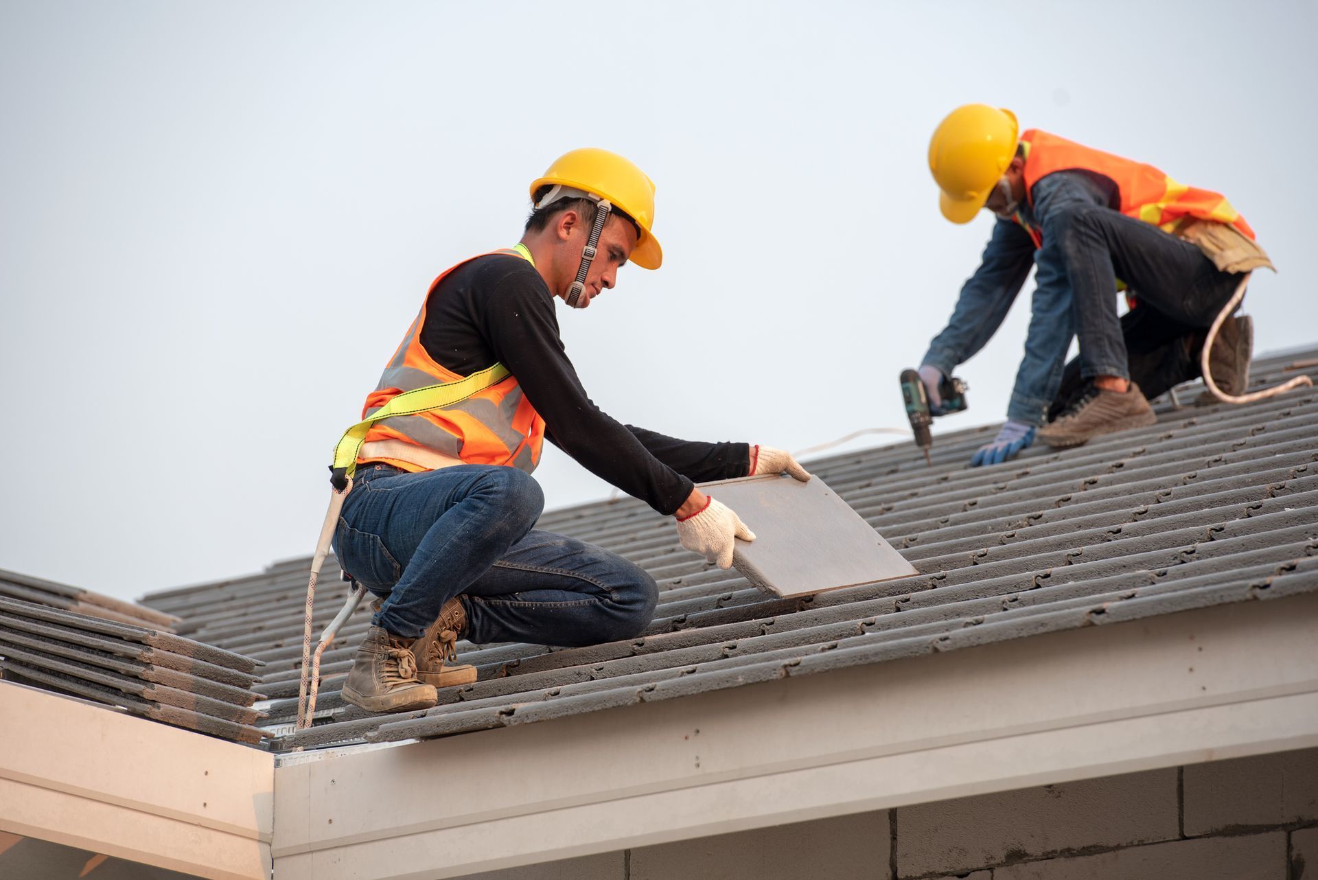 Two roofers in hard hats installing shingles on a house roof