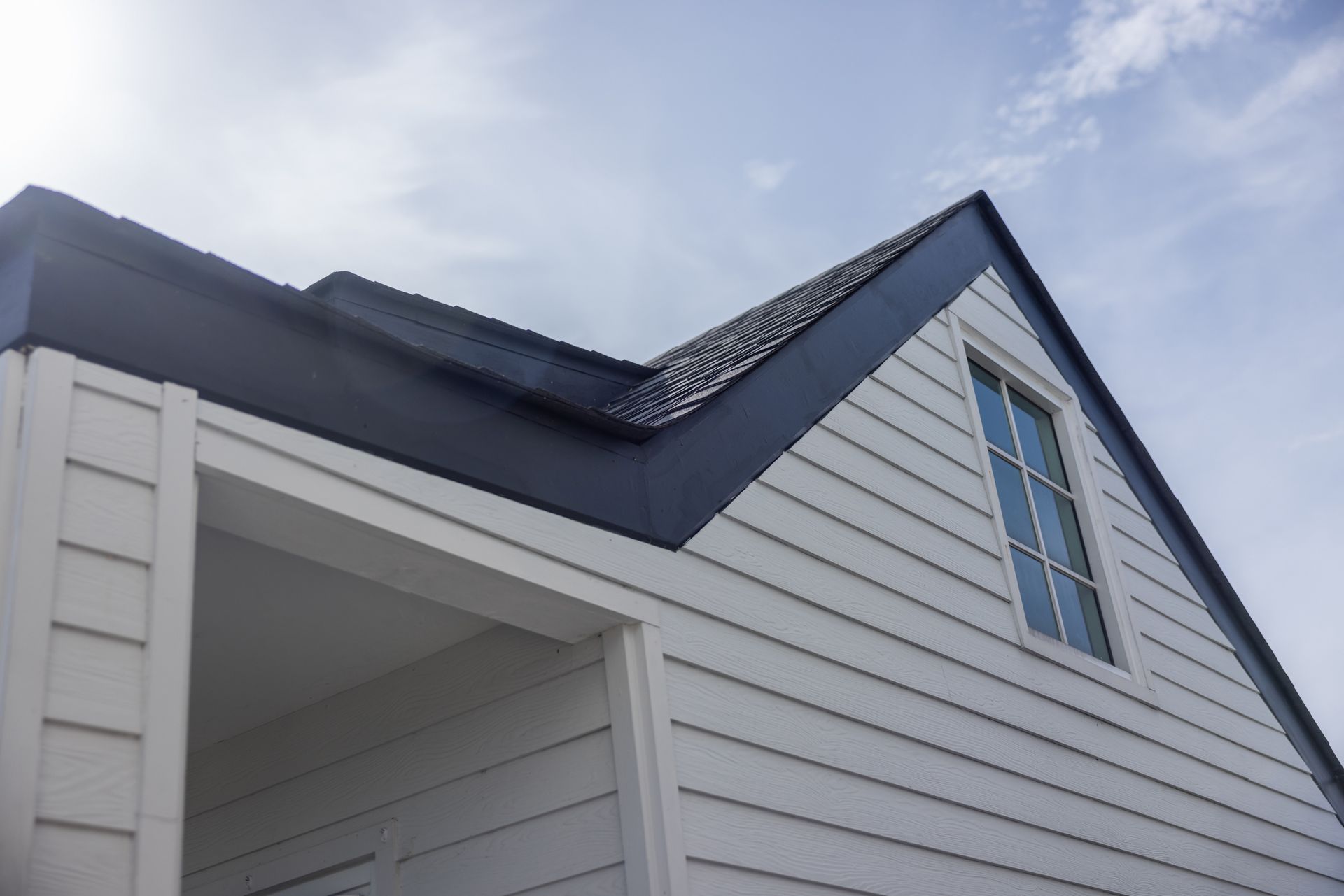 White house gable with dark blue roof and trim against a cloudy sky