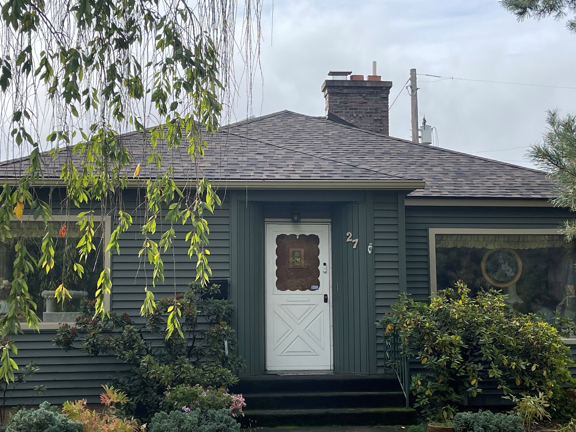Gray shingled roof with two triangular dormer windows against a blue sky and clouds