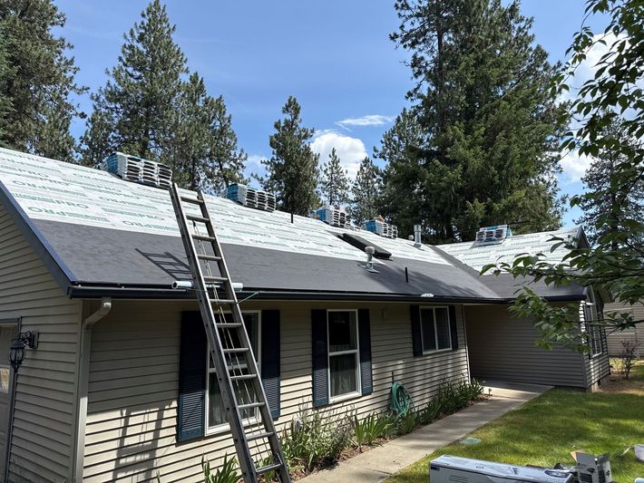 Two roofers installing shingles on a sloped roof, one in a gray shirt and one in a purple shirt. Two roofers installing shingles on a sloped roof, one in a gray shirt and one in a purple shirt.