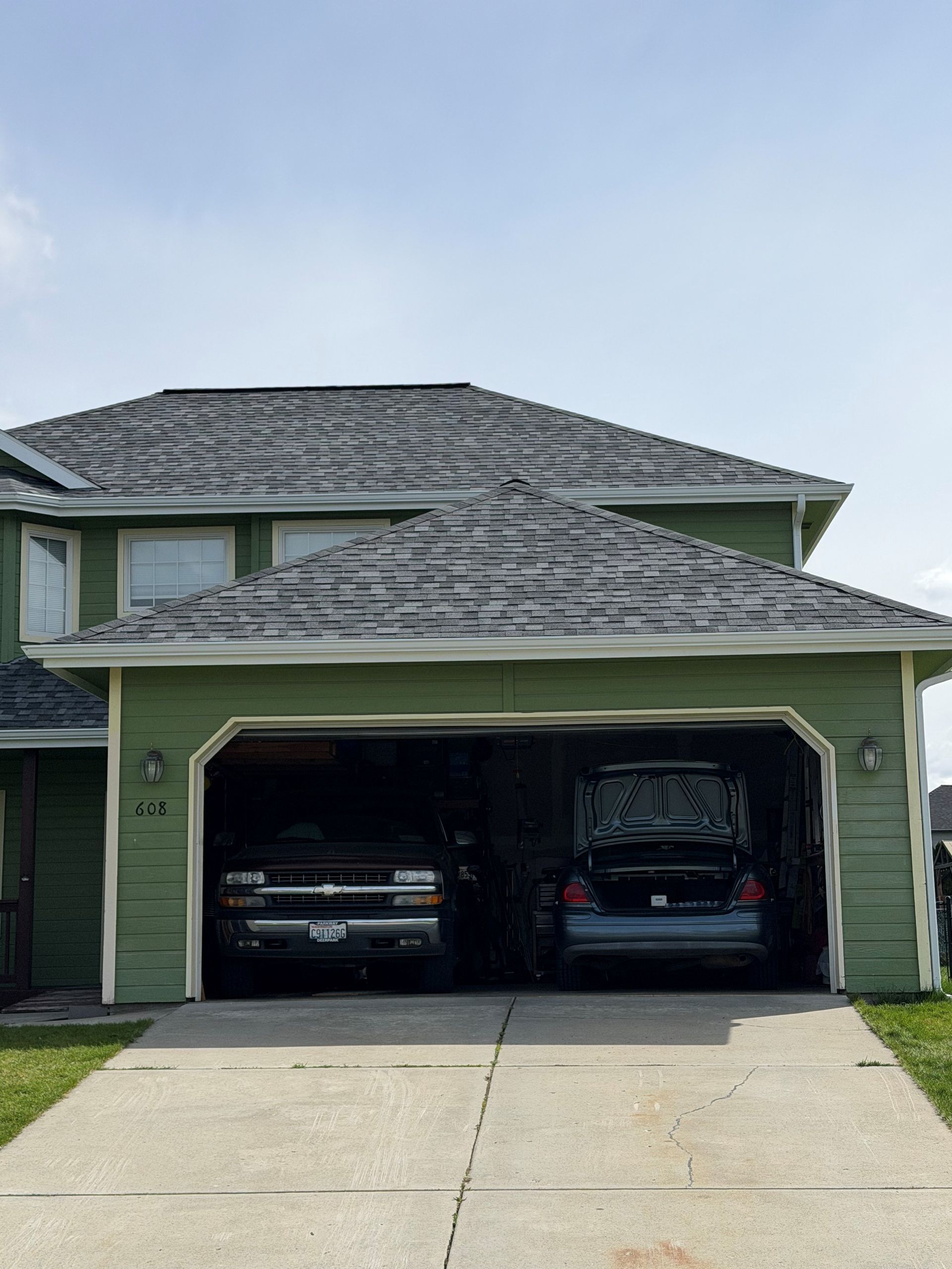 Two-car garage with two vehicles parked inside a green house exterior