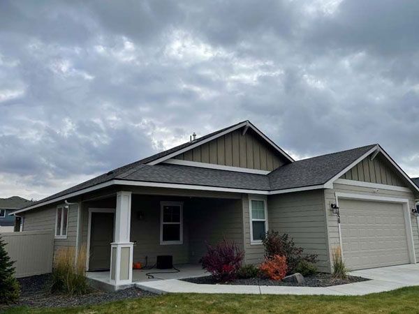 Suburban single-story house with gray siding, white trim, and a two-car garage under cloudy skies