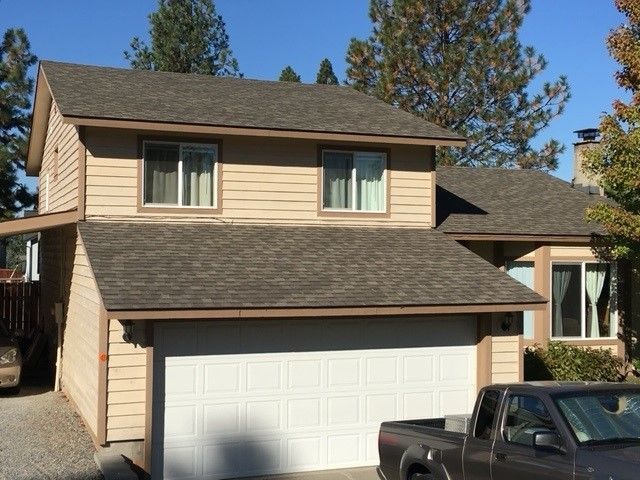 Two-story beige house with brown roof, white garage door, and parked truck in front