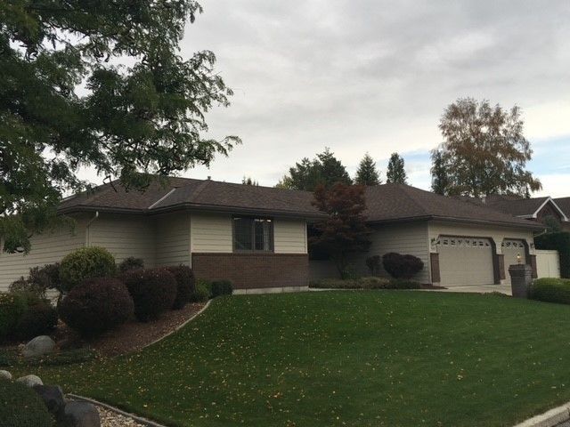 Suburban house with brick front, white garage, and a sloped green lawn under cloudy sky