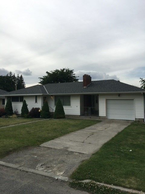 Suburban single-story house with white siding, a garage, and a driveway under a cloudy sky