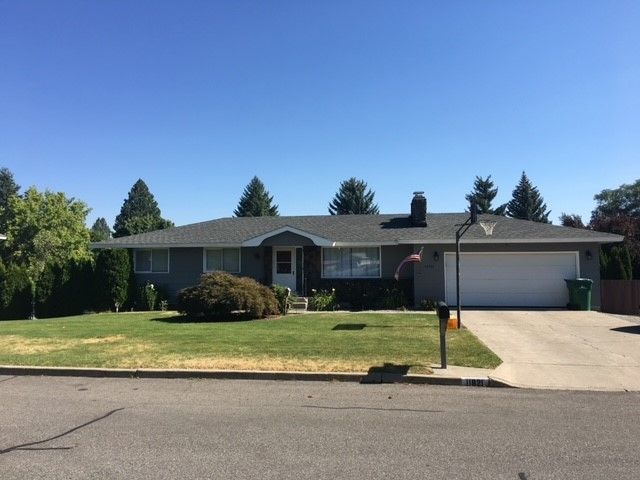 Suburban single-story house with attached garage, front lawn, and driveway under a clear blue sky