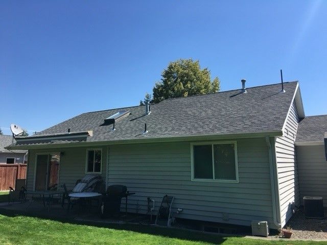 Single-story gray house with a small patio and deck chairs under a blue sky