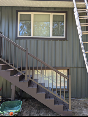 Exterior apartment stair with brown railings, windows, and a ladder leaning on the right side.