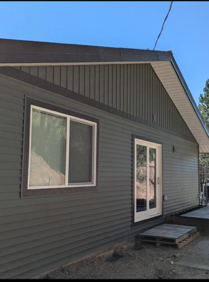 Gray house exterior with a window, white French doors, and a small wooden step under a blue sky
