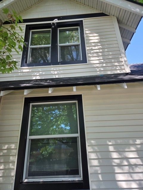 Two black-trimmed windows on a beige house exterior beneath the roof eave