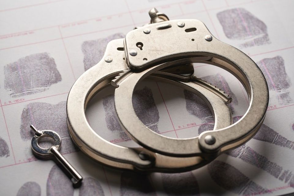 A pair of handcuffs and a key on top of a piece of paper with fingerprints.