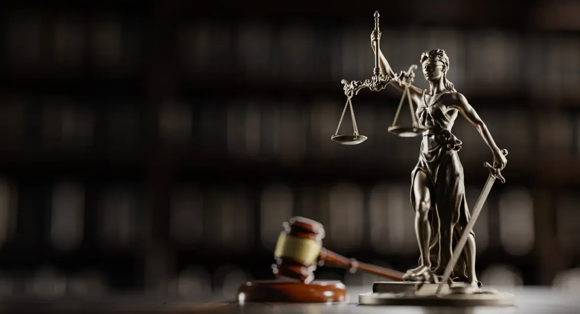 A statue of justice holding scales of justice and a gavel on a table.