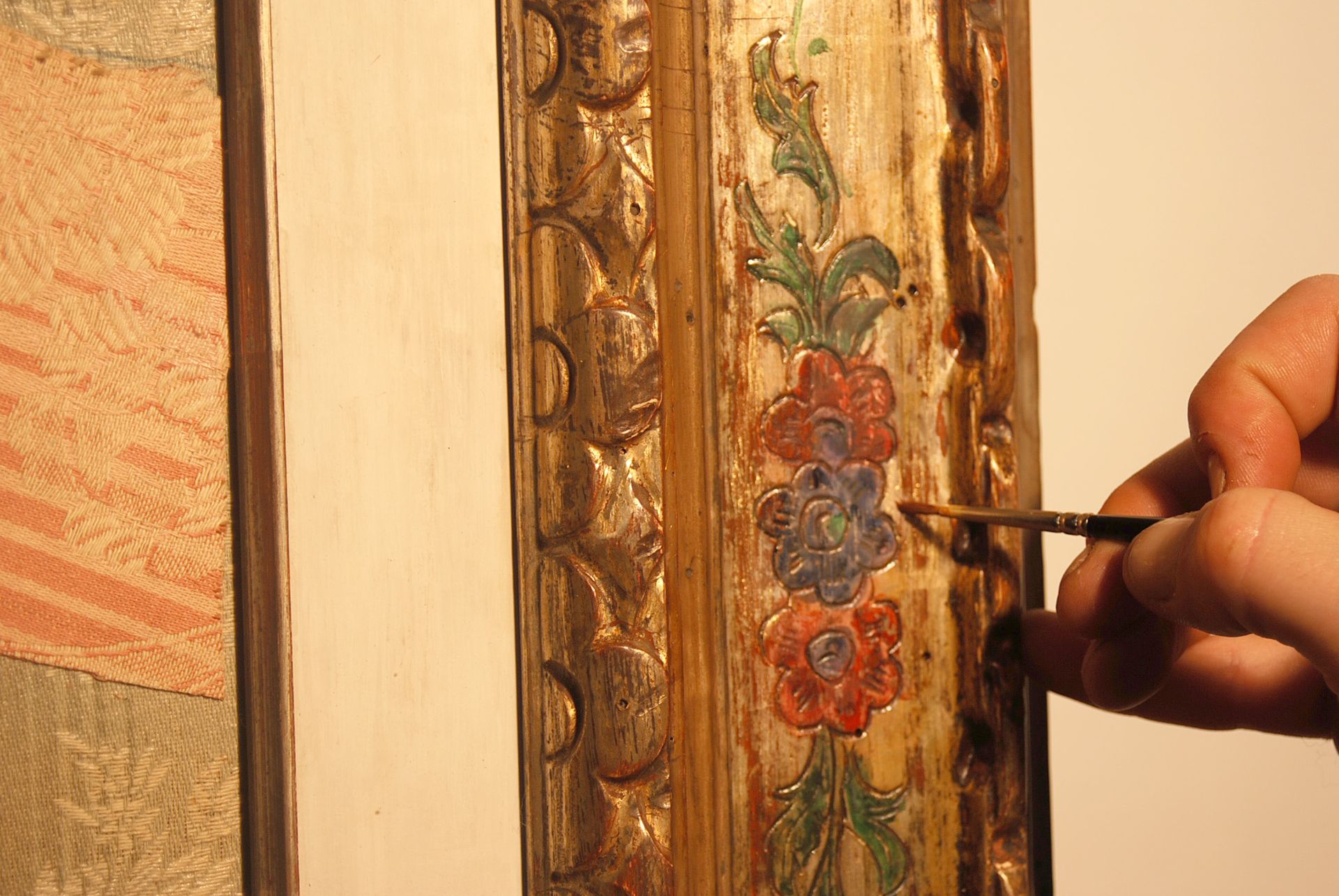 Dipingo a mano i dettagli di un'opera floreale con cornice dorata e riccamente decorata, utilizzando un pennello sottile.