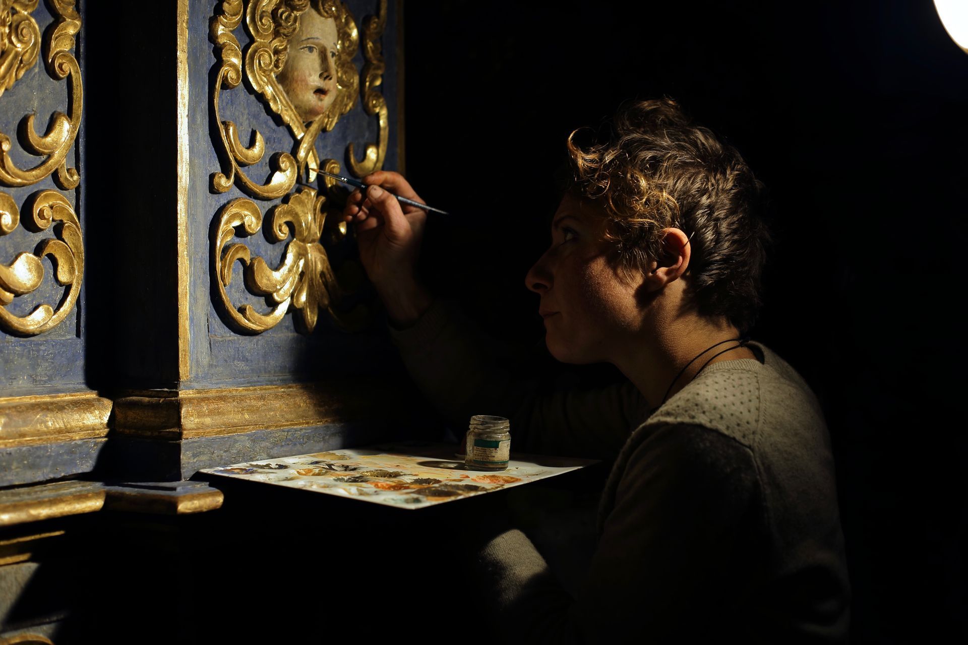 Artista che dipinge un elaborato pannello murale blu e oro in penombra