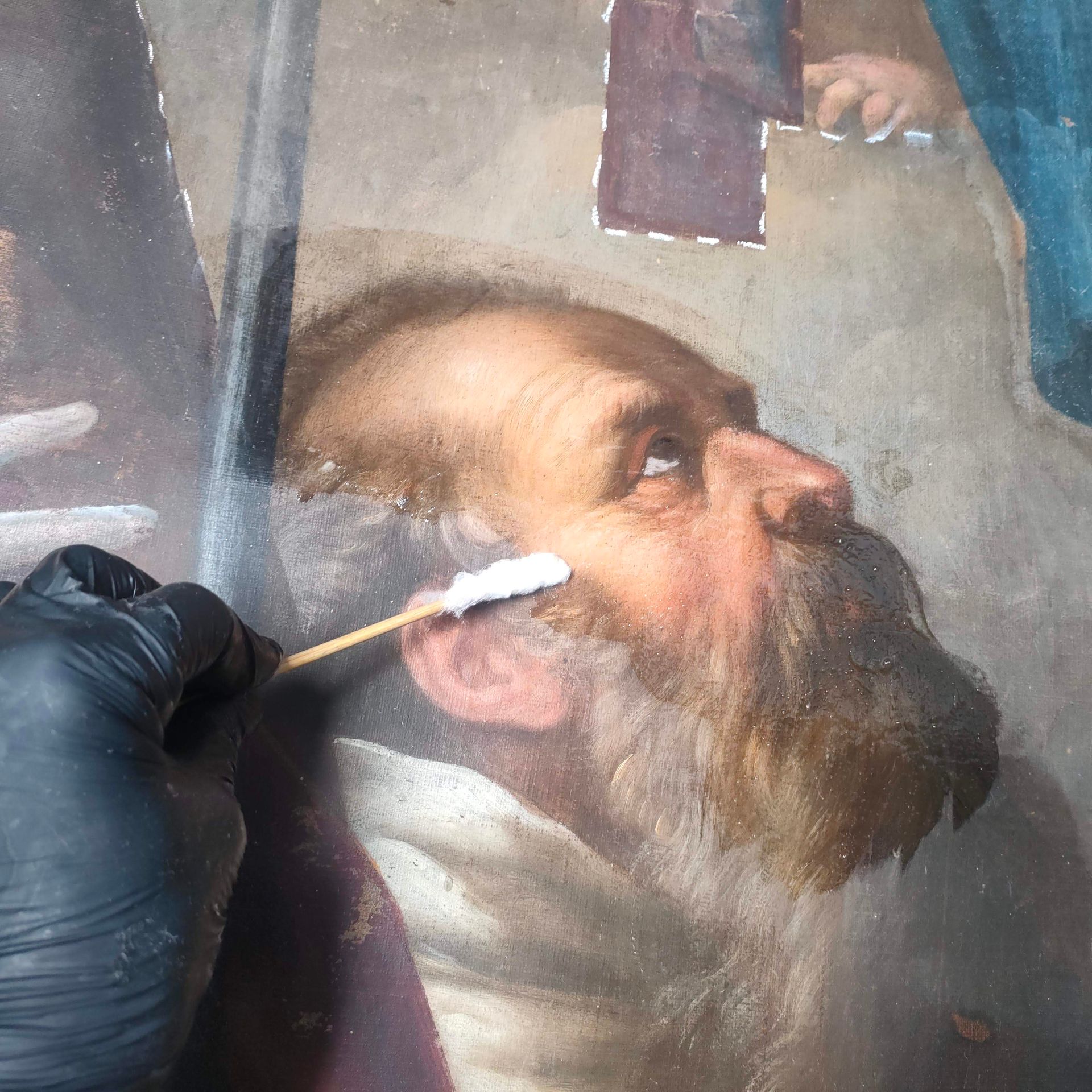 Mano guantata che pulisce un ritratto dipinto di un uomo barbuto su un muro