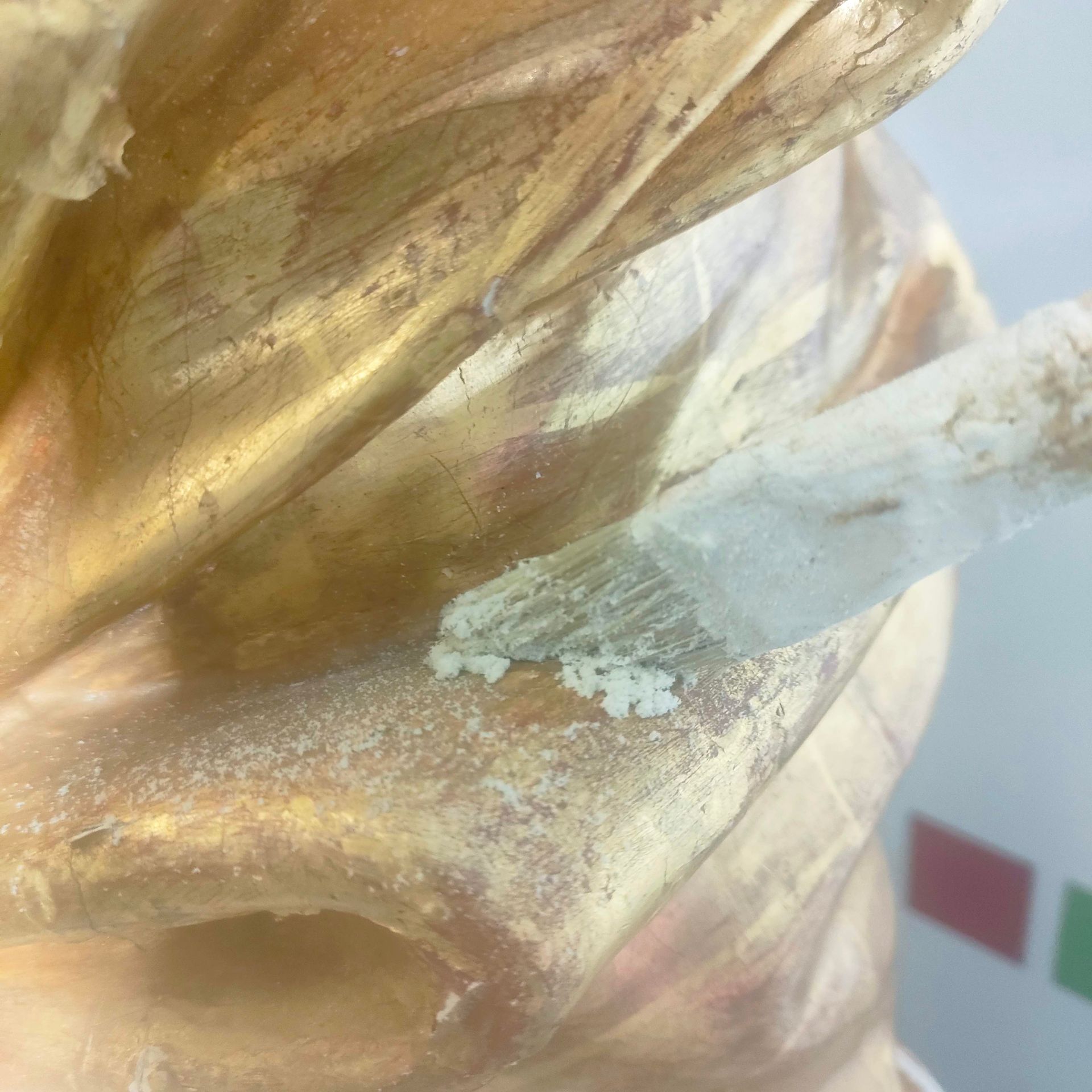 Primo piano di un oggetto dorato traslucido con un'asta bianca, su uno sfondo sfocato con quadrati colorati.