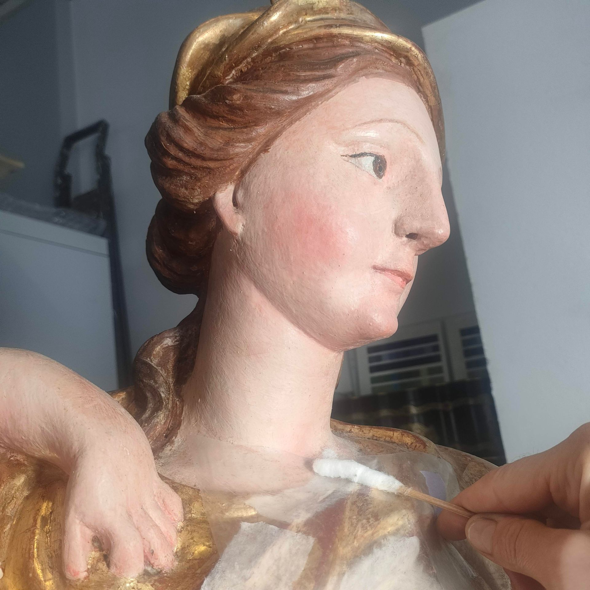 Primo piano della testa e delle spalle di una scultura dipinta, con delle mani che sistemano una copertura di plastica trasparente.