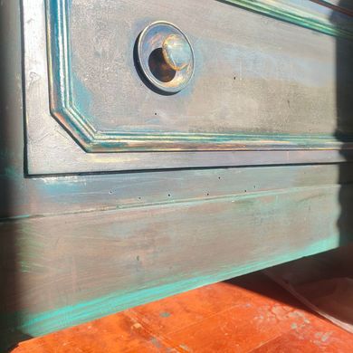 Primo piano del frontale di un cassetto verniciato color verde acqua con una manopola rotonda in metallo sopra una superficie arancione