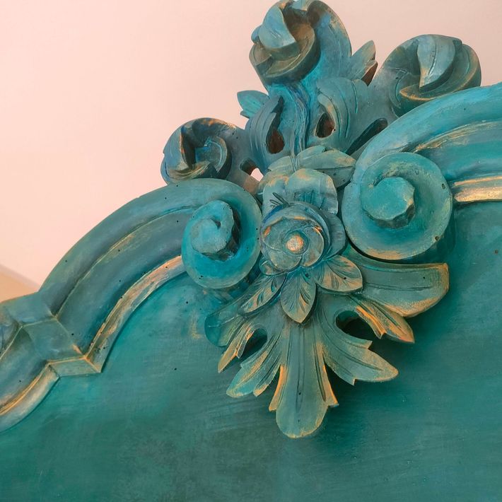 Ornamento floreale in legno intagliato turchese su sfondo rosa pallido.