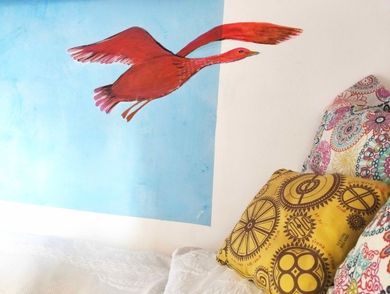 Murale con uccelli rossi sopra un letto con cuscini decorati su una parete bianca e blu