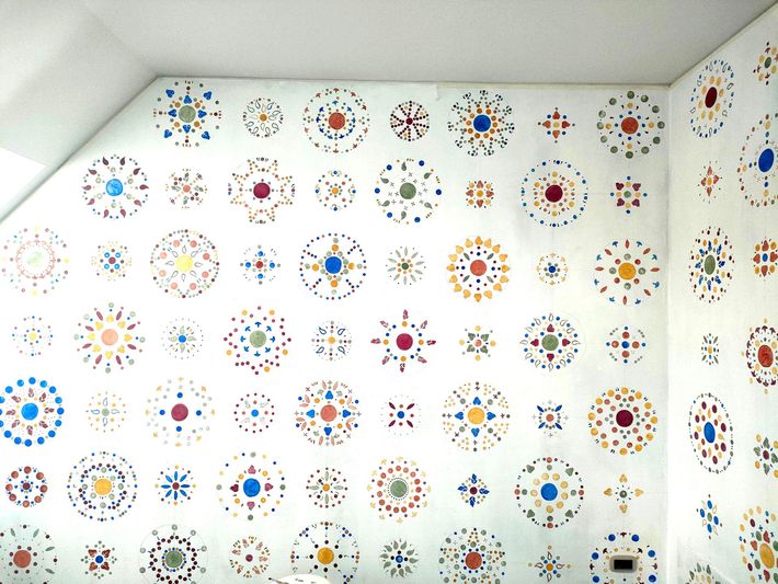 Le pareti bianche della stanza sono ricoperte di adesivi colorati a motivi circolari disposti a griglia.