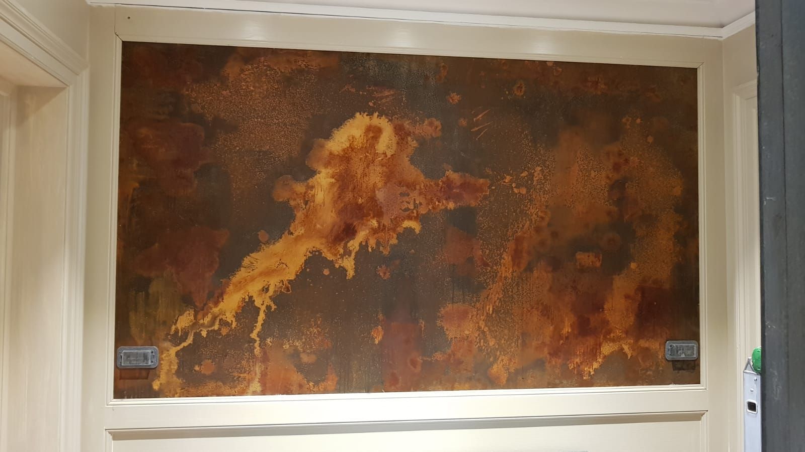Grande dipinto astratto murale color ruggine con tonalità arancioni e marroni, appeso all'interno tra le porte.