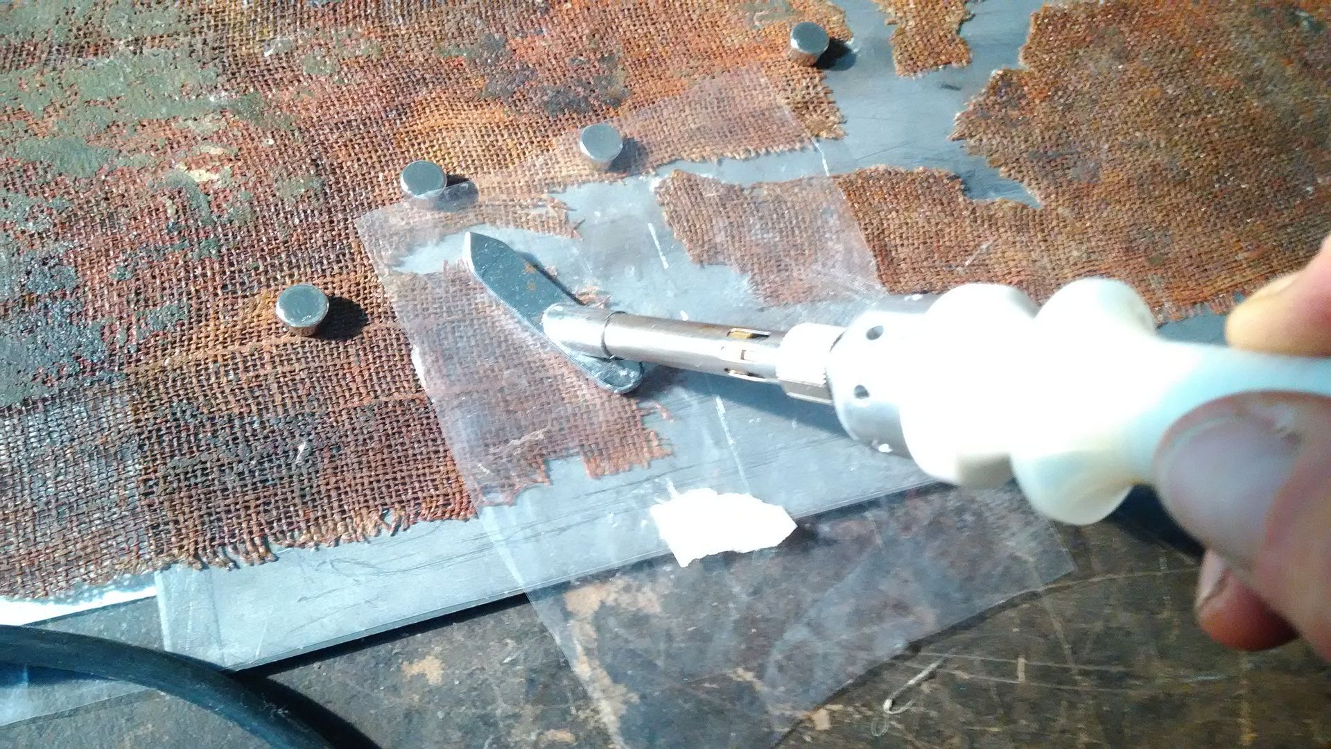 Una mano usa un taglierino per tagliare del nastro adesivo trasparente su una superficie metallica color ruggine.