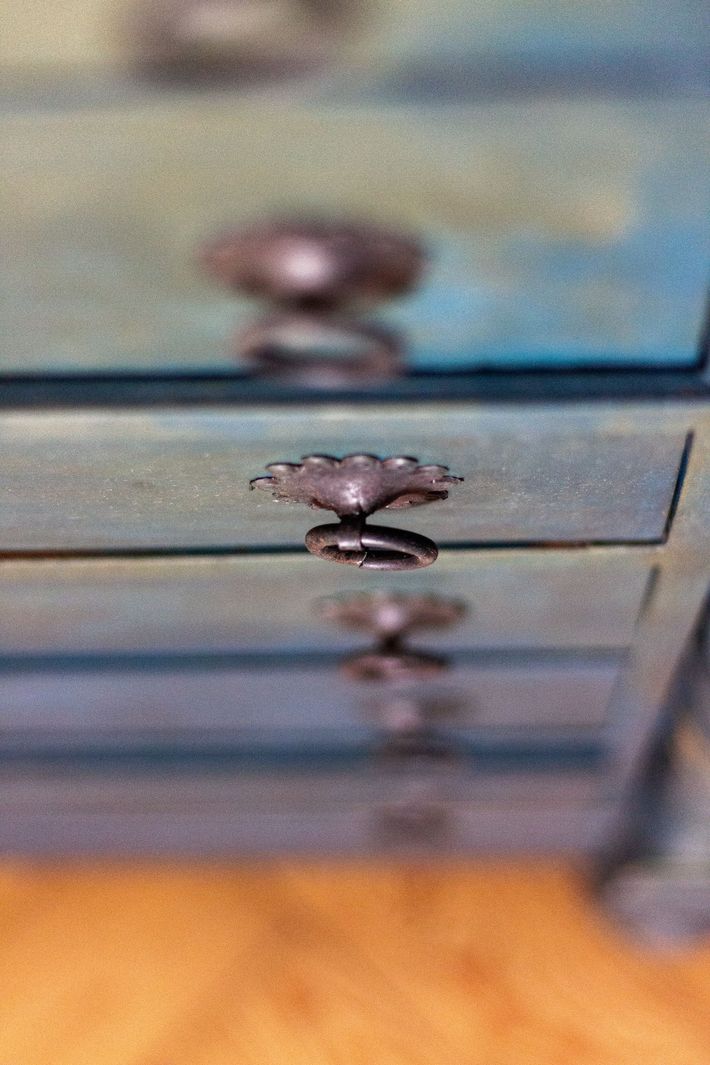 Primo piano di un cassetto blu di una cassettiera con una piccola maniglia in metallo e il pavimento in legno sottostante.