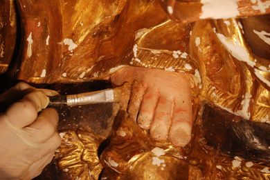 Una mano che impugna un pennello dipinge un piccolo piede d'oro in una scena artistica ravvicinata.