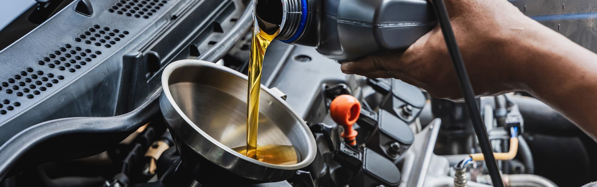 Filling engine oil into a car's engine with a funnel.