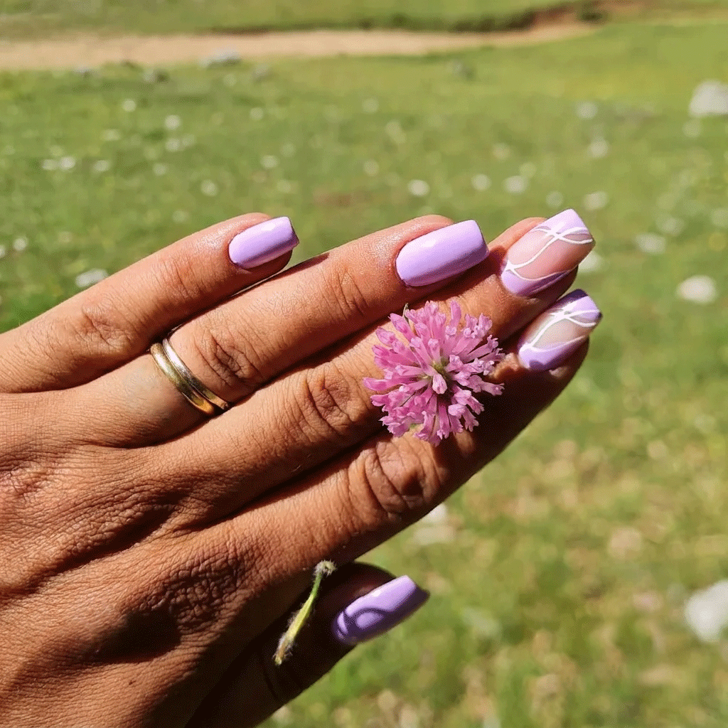 Una mano con le unghie color lavanda che stringe un fiore rosa sopra un campo erboso.
