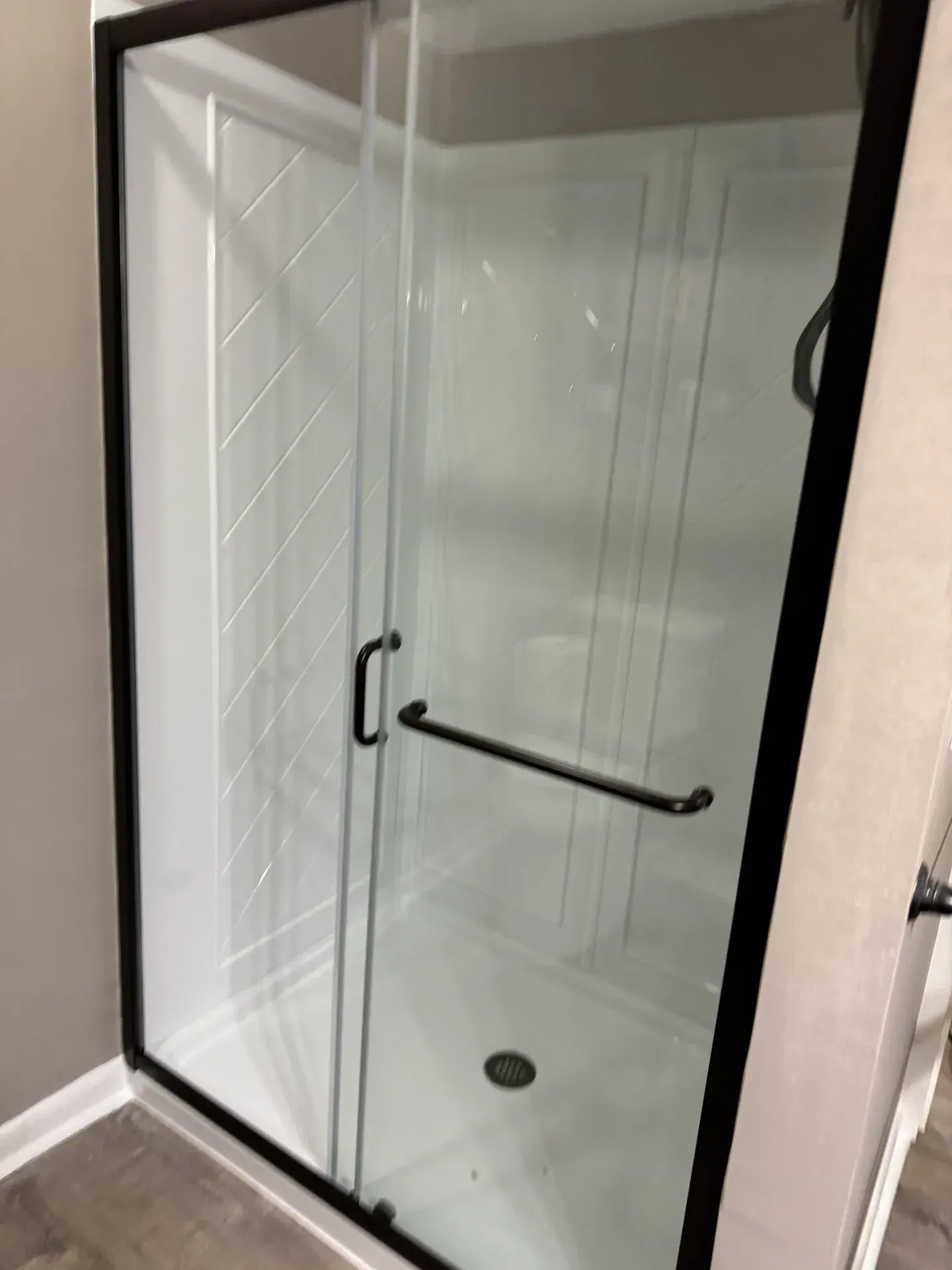 Glass shower enclosure with black trim, white walls, and dark metal handle.