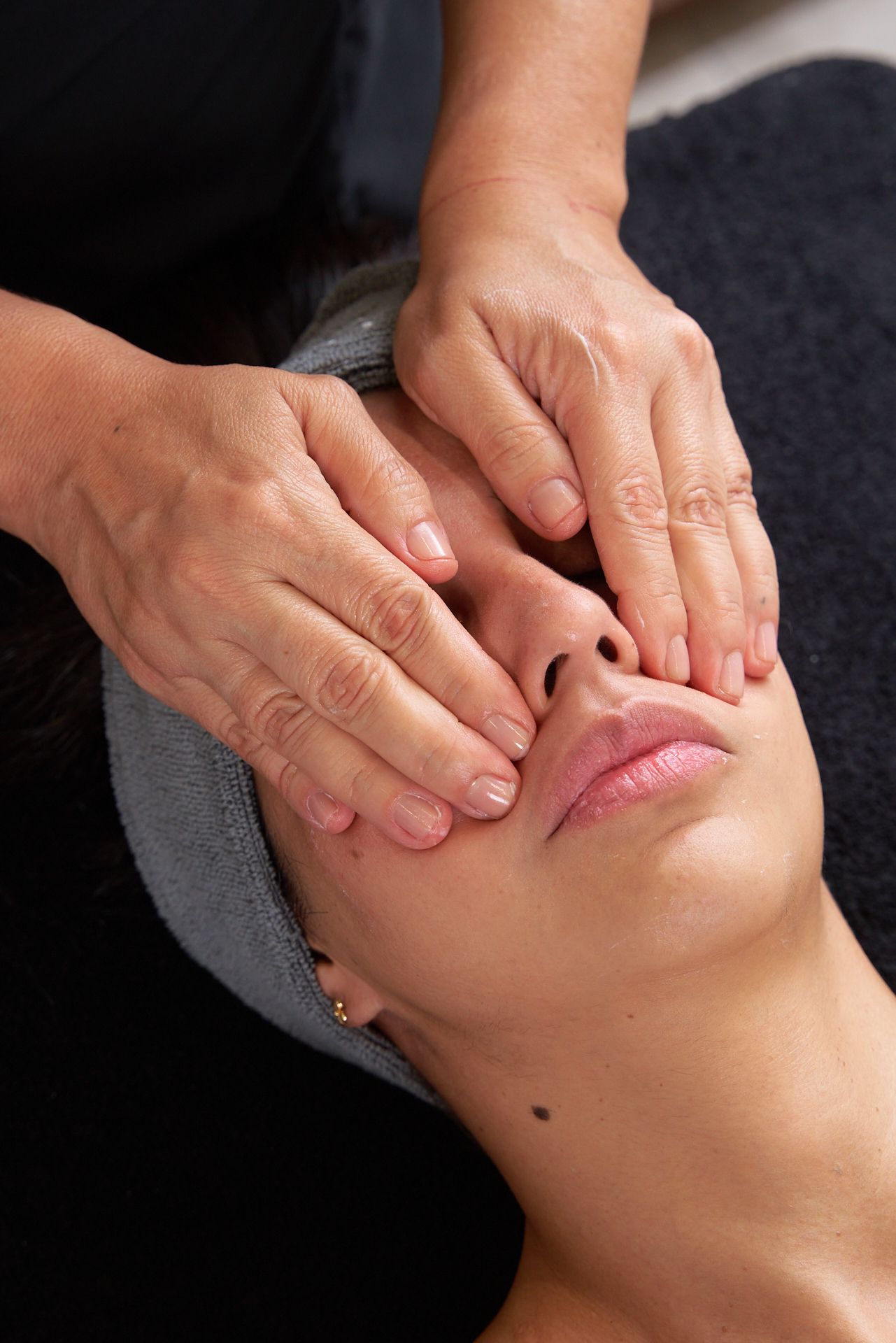 Manos que dan un masaje facial a una persona recostada con los ojos cerrados.