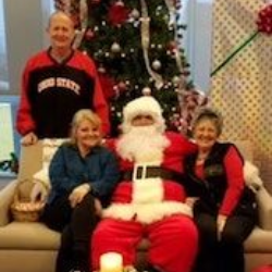 Santa seated with three people in front of a Christmas tree and holiday decorations