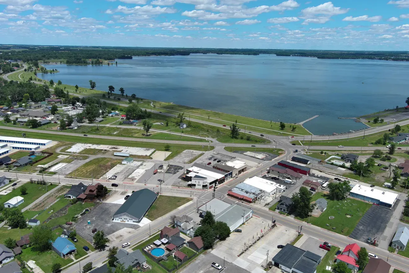 Aerial view of a lakeside town with homes, streets, and a large blue lake under a partly cloudy sky