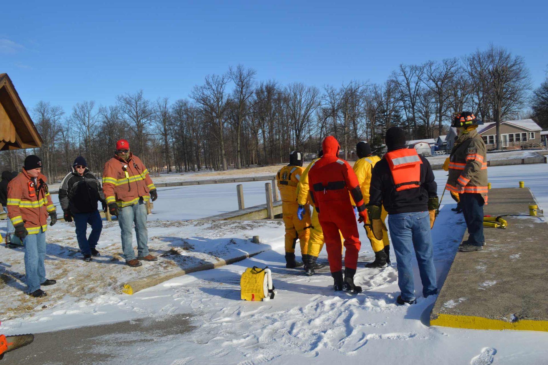 Workers in safety vests gather around a snow-covered roadside work site.