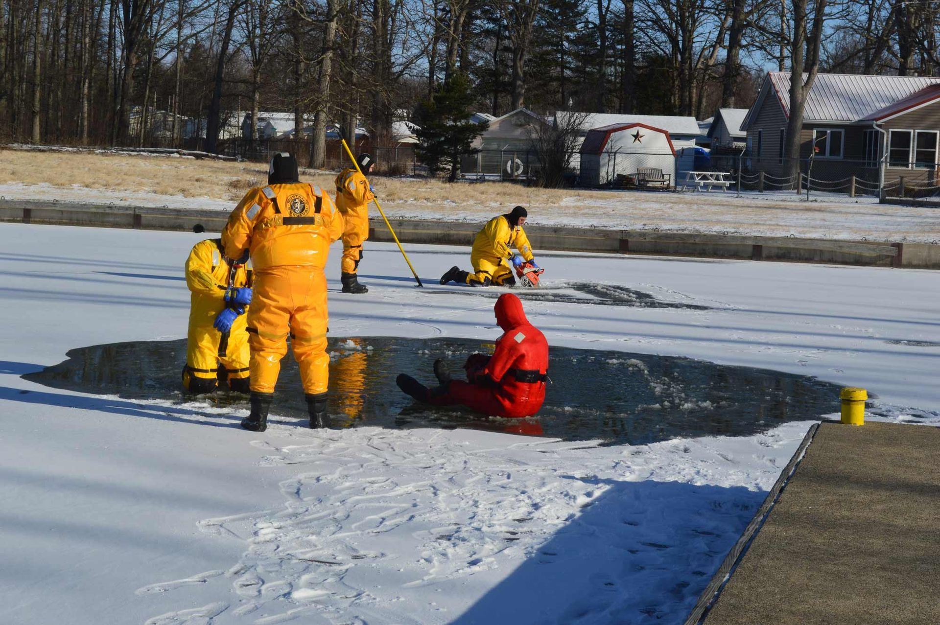 Rescue workers in yellow and red dry suits at an ice hole on a frozen lake with a rescue line