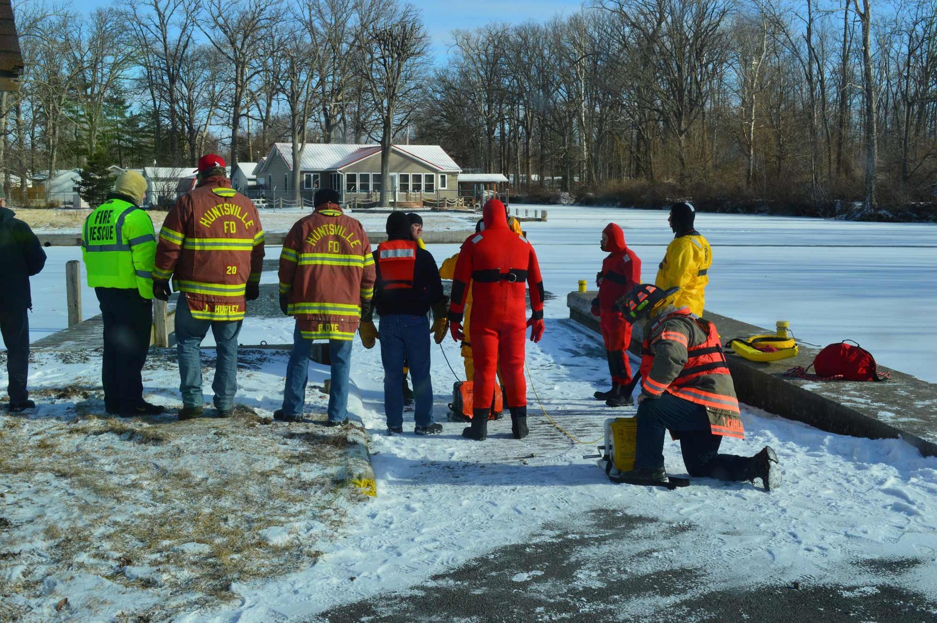 Rescue crew in bright gear standing on a frozen lake beside a red sled and rescue equipment