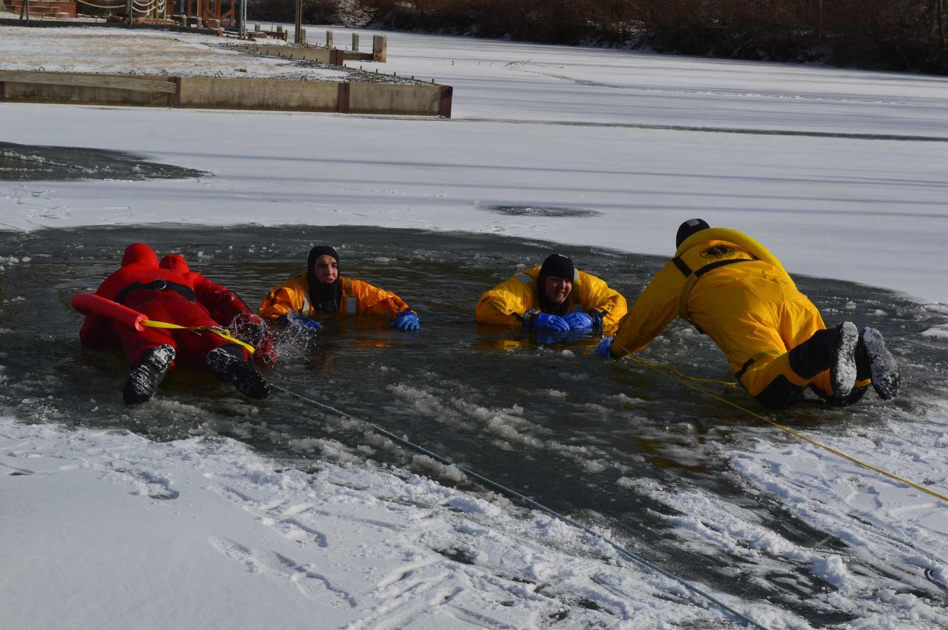 People in bright jackets lie on an icy river, practicing a rescue drill