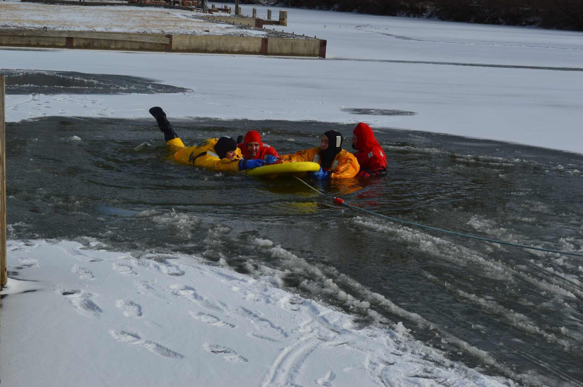 Kayakers in yellow and red gear paddle through icy water near the shoreline