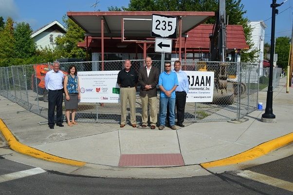 Four men standing on a sidewalk behind a fence near a street sign and building at a corner.