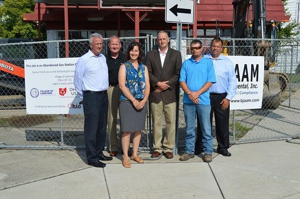 Five people standing together outdoors in front of a construction site fence and signage.