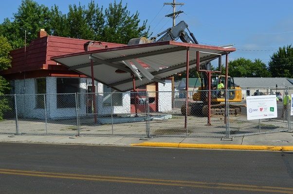 Street-side bus stop shelter with a red roof and a sign by the curb, beside a chain-link fence.