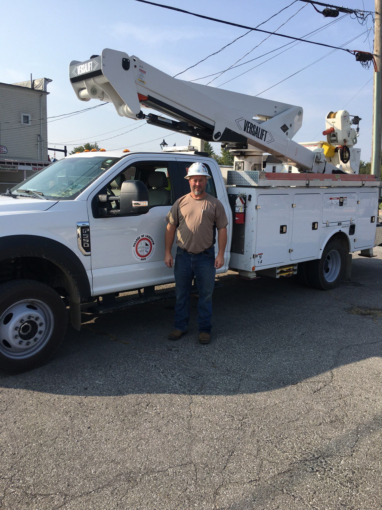 Utility truck with bucket lift parked outdoors, with a worker standing beside it under a clear sky.