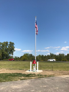 American flag on a tall pole at a roadside memorial with a red tribute marker and flowers