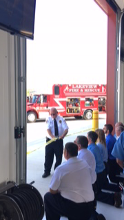 Firefighters and bystanders gathered in a fire station bay, watching a red fire truck outside.